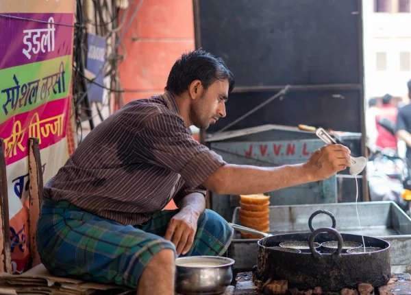 A man prepares traditional street food, frying dough in hot oil at a busy food stall in Jaipur.