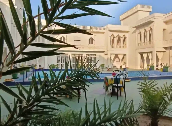 A savista retreat showcases a stunning white edifice with arched windows and a domed roof, nestled in a lush tropical haven of palms. Surrounded by vibrant greenery, it presents a serene and enchanting escape amid the vast savanna.