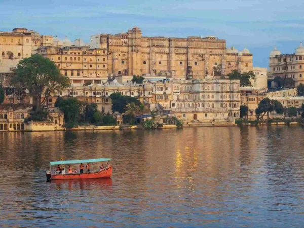 The image showcases a wide, serene view of the Udaipur City Palace complex, as seen from Lake Pichola in Rajasthan, India.