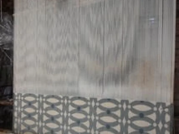 A high angle close-up shot the vertical threads of a loom. The lower portion of the loom displays a partially completed textile with a repeating pattern of interlocking circles in light blue and white against a white background