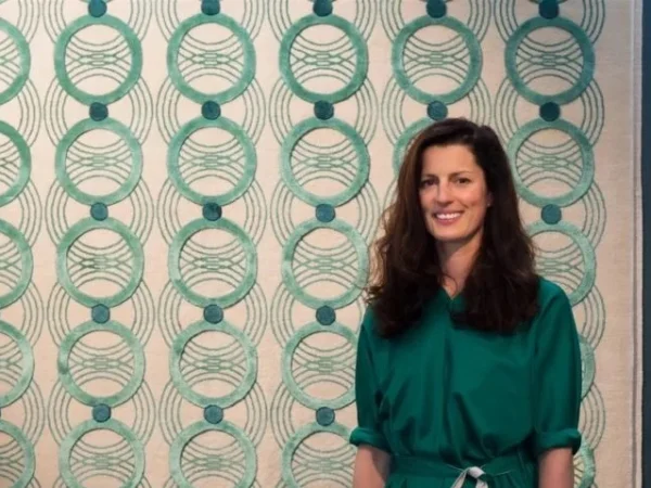 Woman in green, standing in front of the rug with the interlocking pattern.