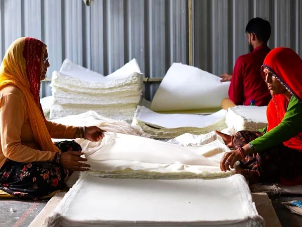 The image features three artisans in a workshop setting, engaged in the production of handmade paper.