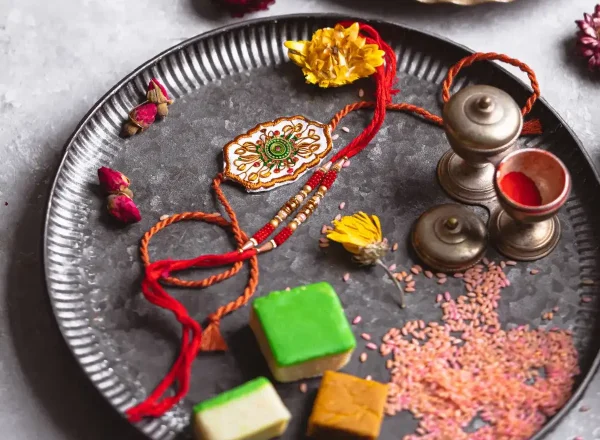 A raksha bandhan displays a vibrant, traditional design, with a fabric rectangle adorned in rich colors and intricate patterns. Wrapping a silver plate with gold and red flowers, silver bells, its a visually stunning symbol of cultural significance during Diwali.
