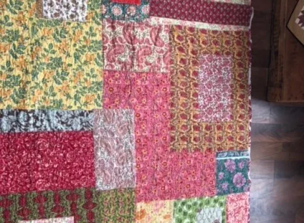 Overhead view of a colorful, hand-stitched patchwork quilt with various floral patterns and geometric block designs, displayed at Savista Retreat.