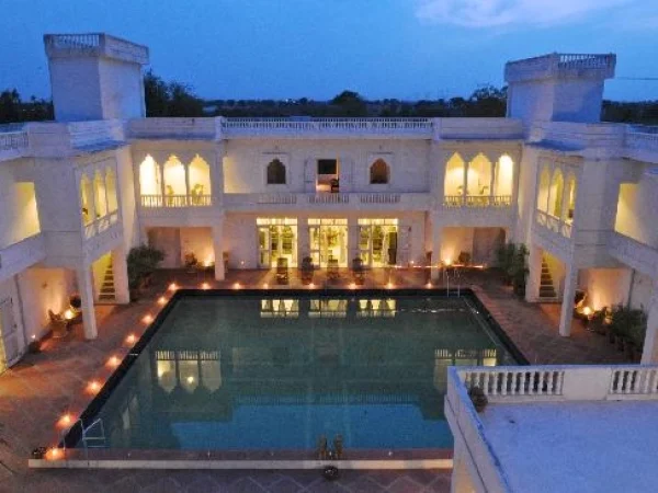 A rectangular pool is surrounded by a white, multi-story building with lit windows and balconies at dusk, capturing the tranquil ambiance of Savista Retreat.