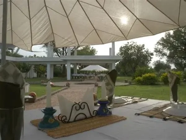 A close-up of an outdoor dining table setup at the Savista Retreat. The table is covered with white linen, featuring elegant place settings with candles, napkins, and woven mats.