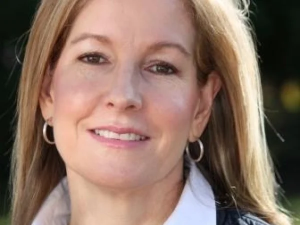 Woman with blonde hair, smiling with silver hoop earrings.